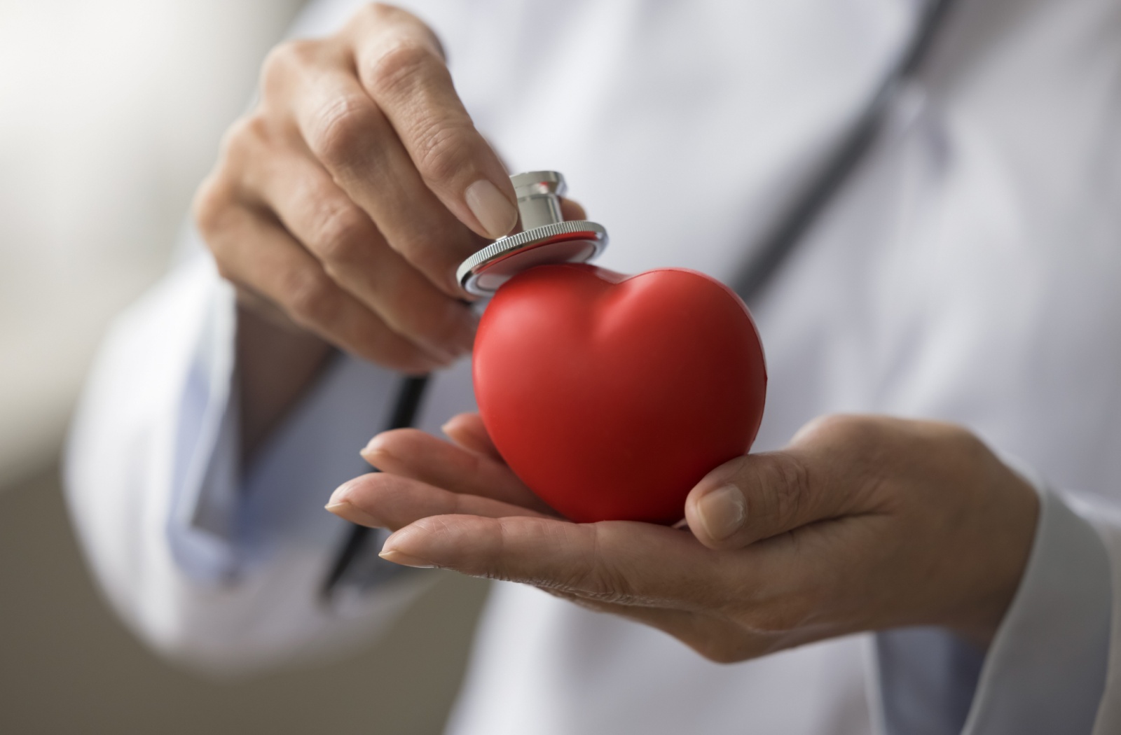 A close-up image of a cardiologist holding a stethoscope to a 3D heart icon.