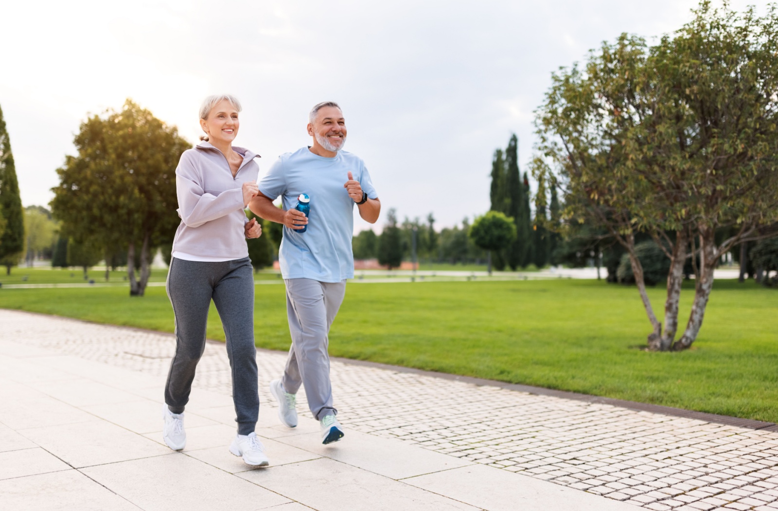 A pair of older adults outside on a walk in the park, smiling as they work on their cardio.