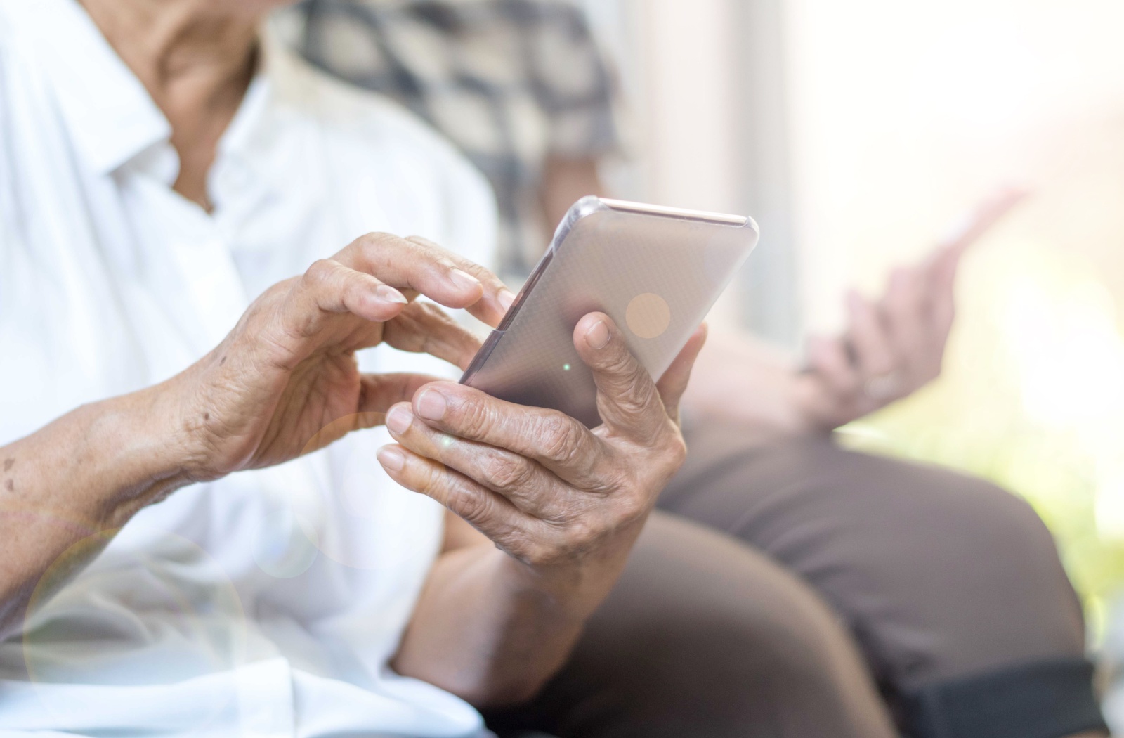 An older adult sitting beside their partner while using their brand-new cell phone.