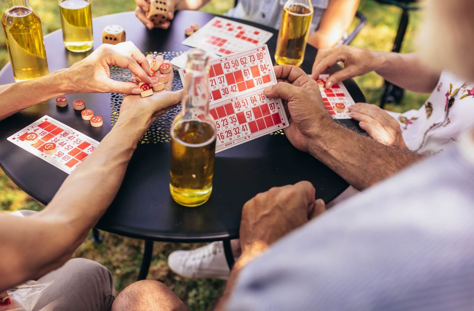 A group of seniors sit around a round table, playing bingo with drinks while outdoors with their community