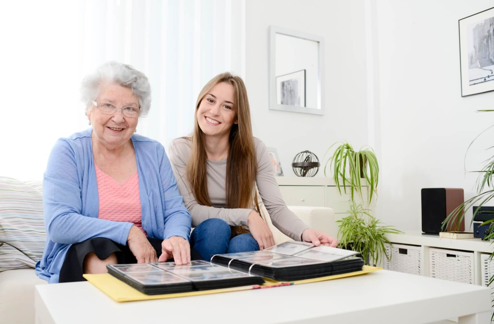 A grandchild visiting a senior with dementia in memory care looks through a photo album with their loved one to connect