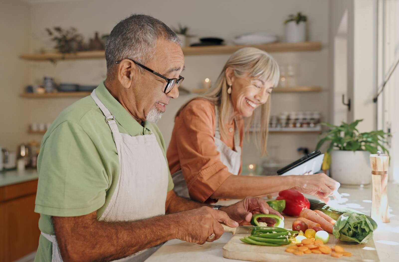 Two older adults smile while chopping vegetables for a meal in independent living
