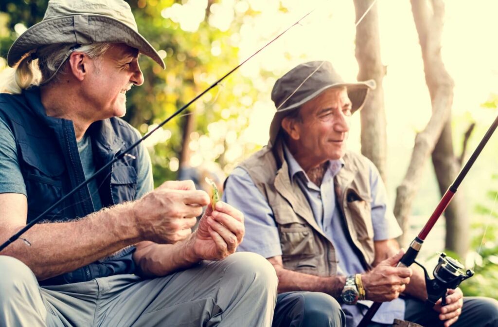 Two older men sitting down while one holds a fishing rod and the other holds a lure