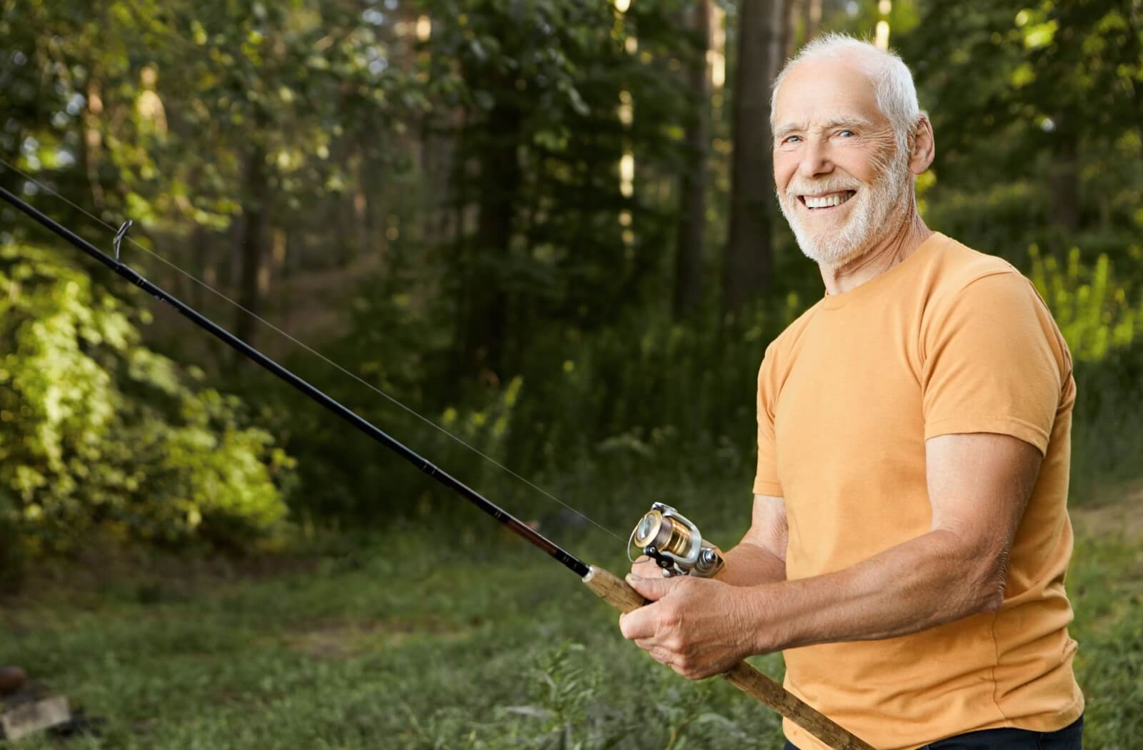 An older man holding a fishing rod and smiling at the camera