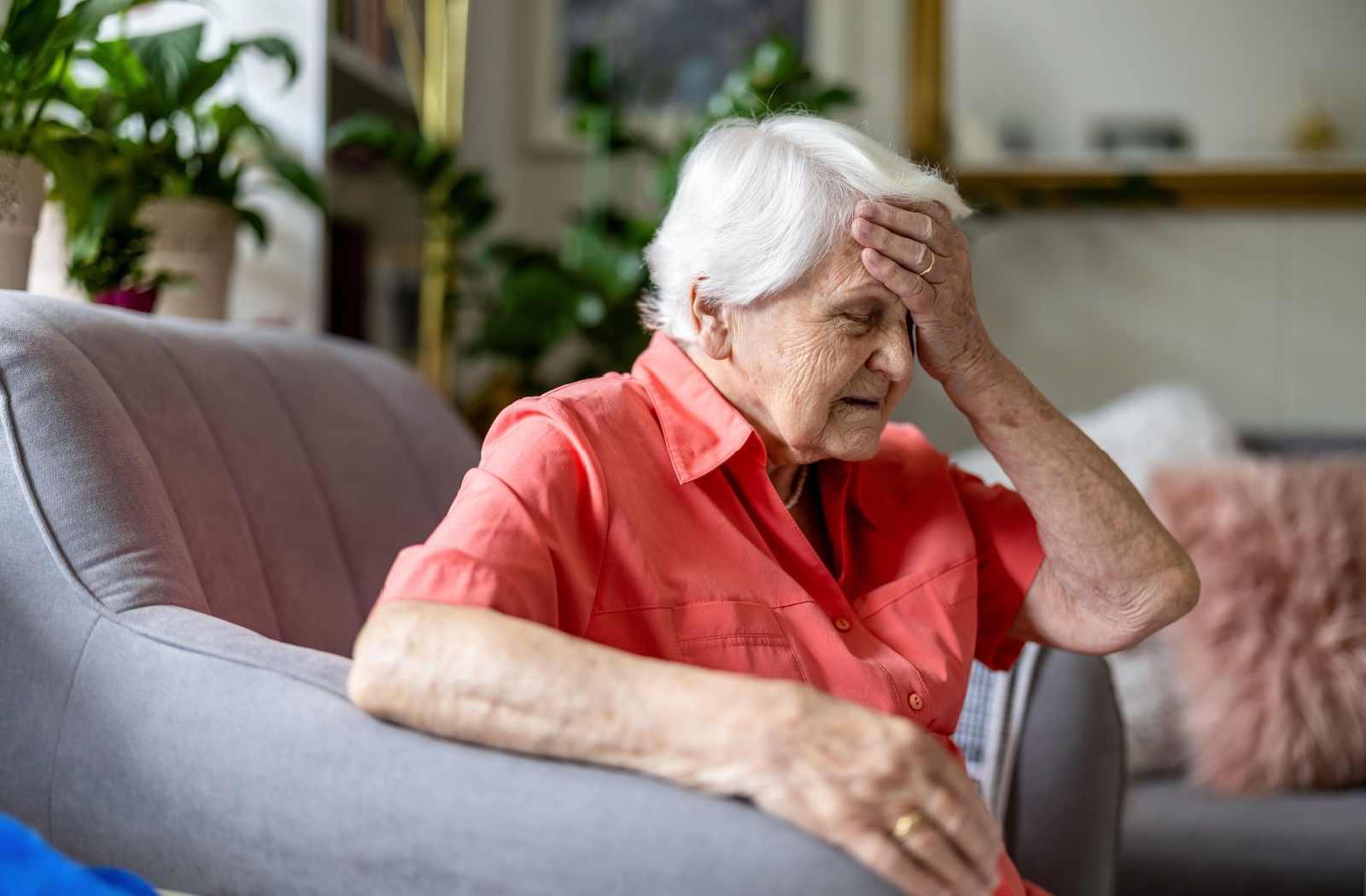 An older adult with dementia sitting in an armchair with their left hand on their forehead.