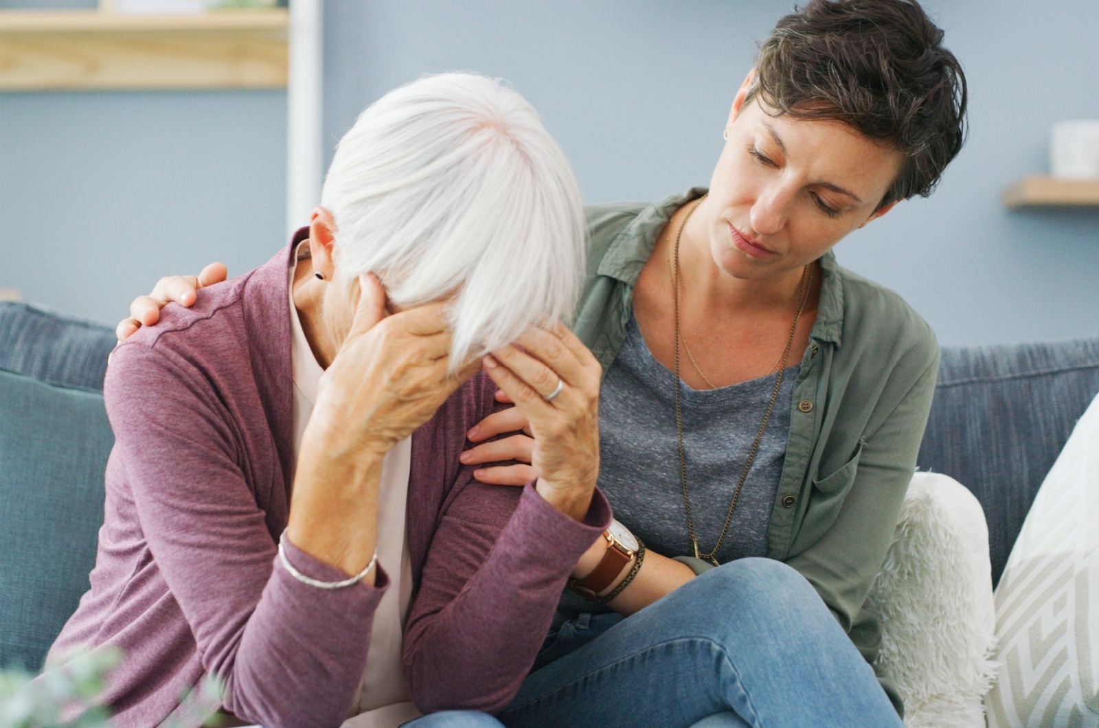 An adult child sitting next to their mom with dementia and comforting them.
