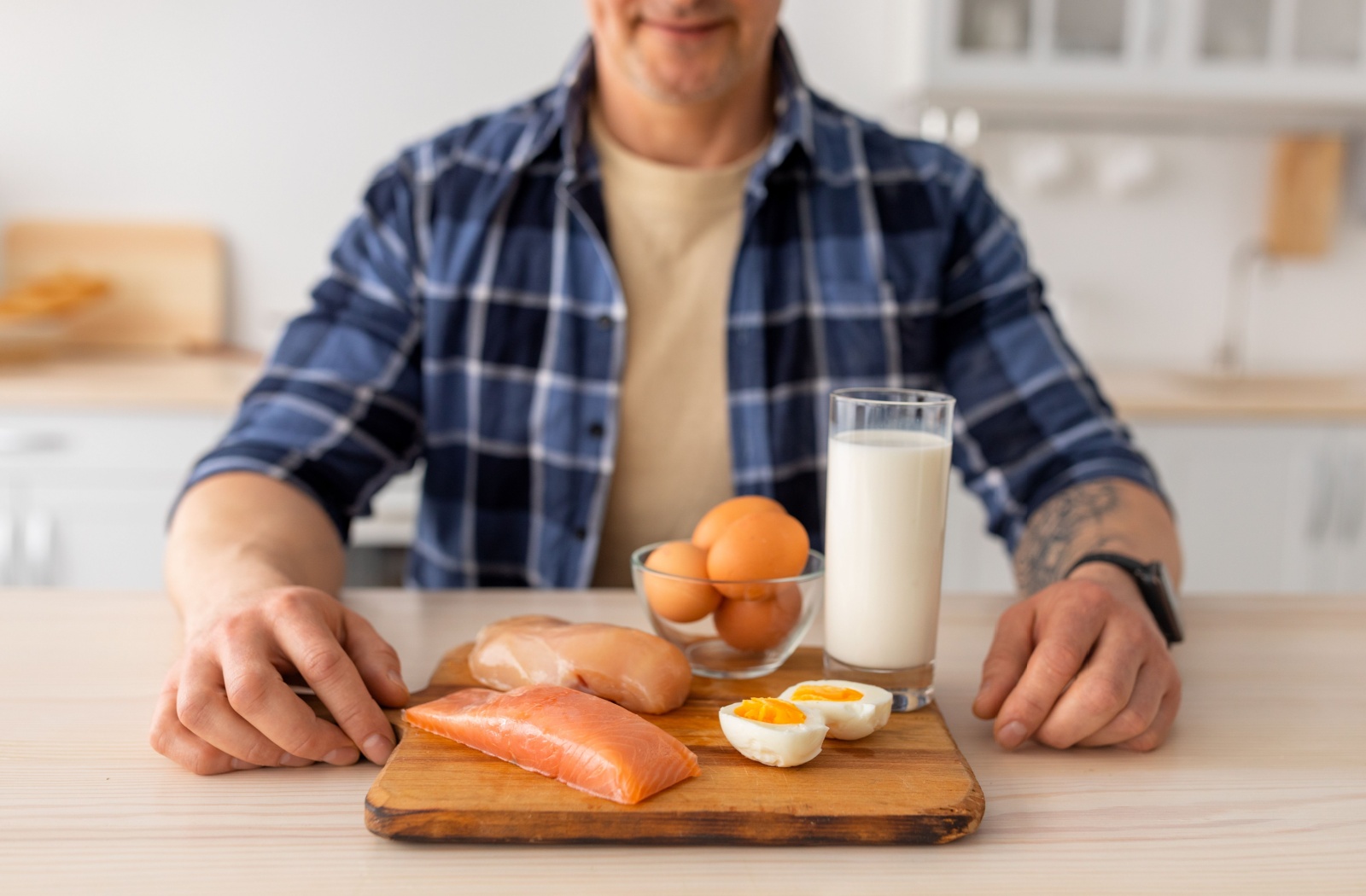 A close-up view of an older adult sitting in front of a spread of eggs, fish, chicken, and a glass of milk.