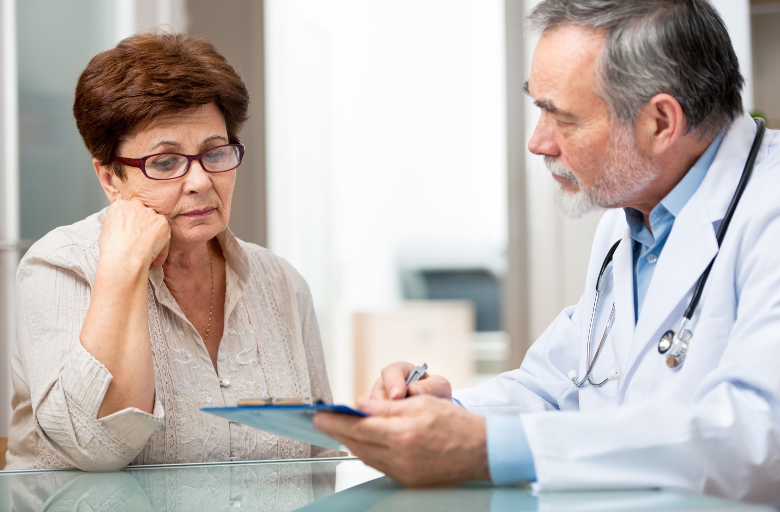 A healthcare provider and older adult seated at a table during a medical evaluation.
