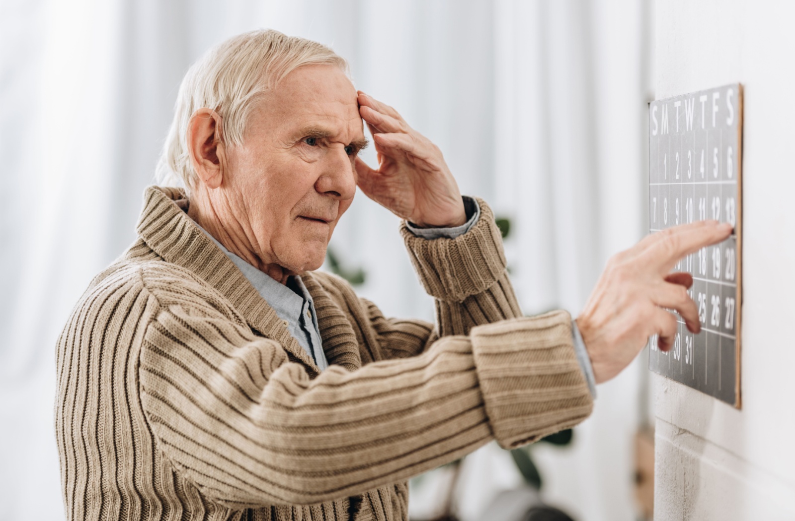 An older adult points with his right hand while he has his left hand to his forehead in confusion.