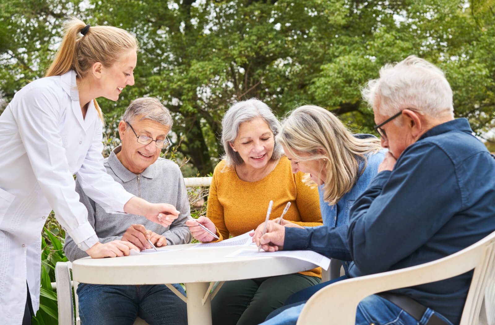 A caregiver helping a group of older adults outside while they play a fun word-based game.