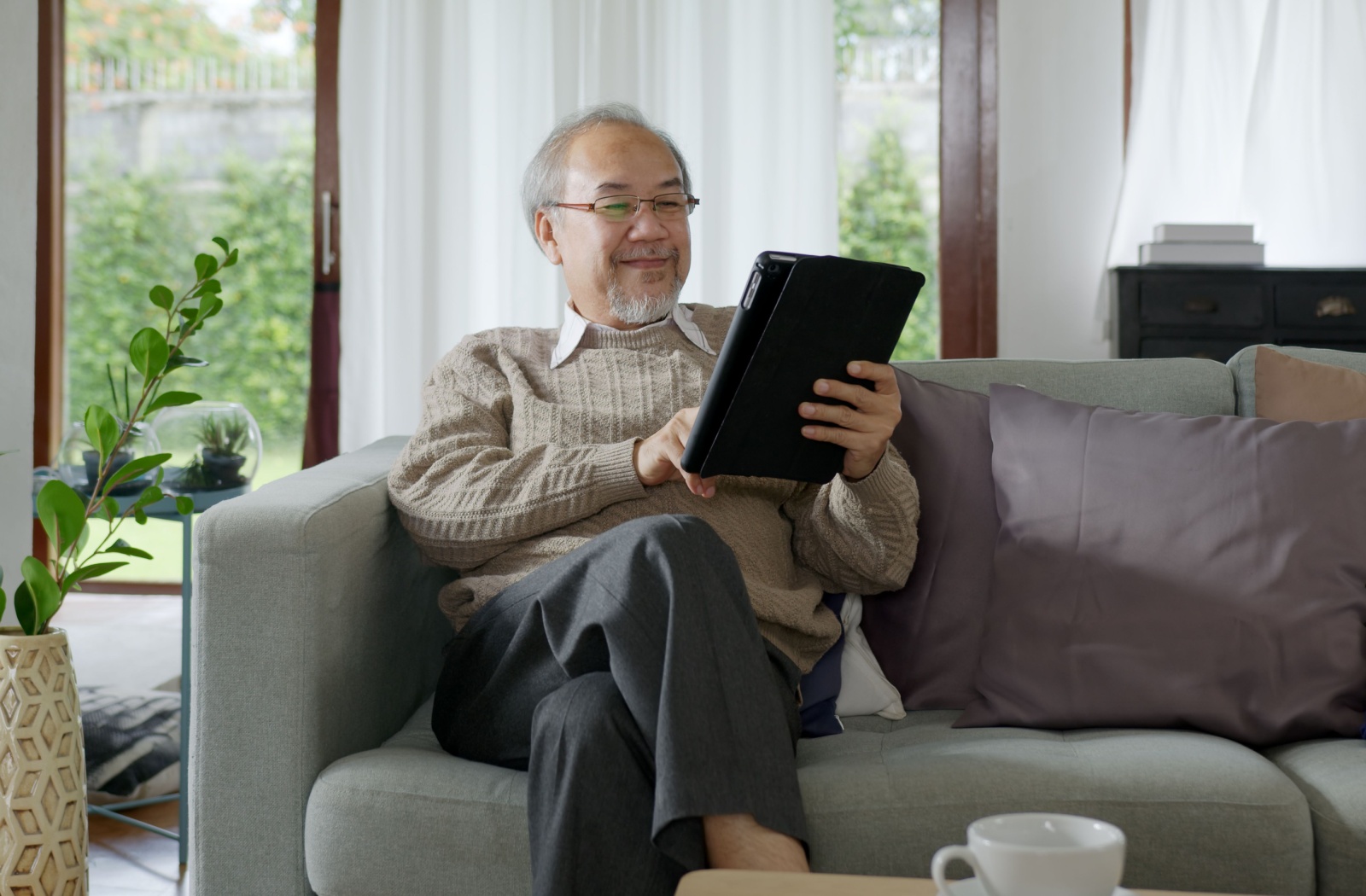 A smiling senior relaxes on their couch and reads one of the top 10 books for seniors on their tablet.