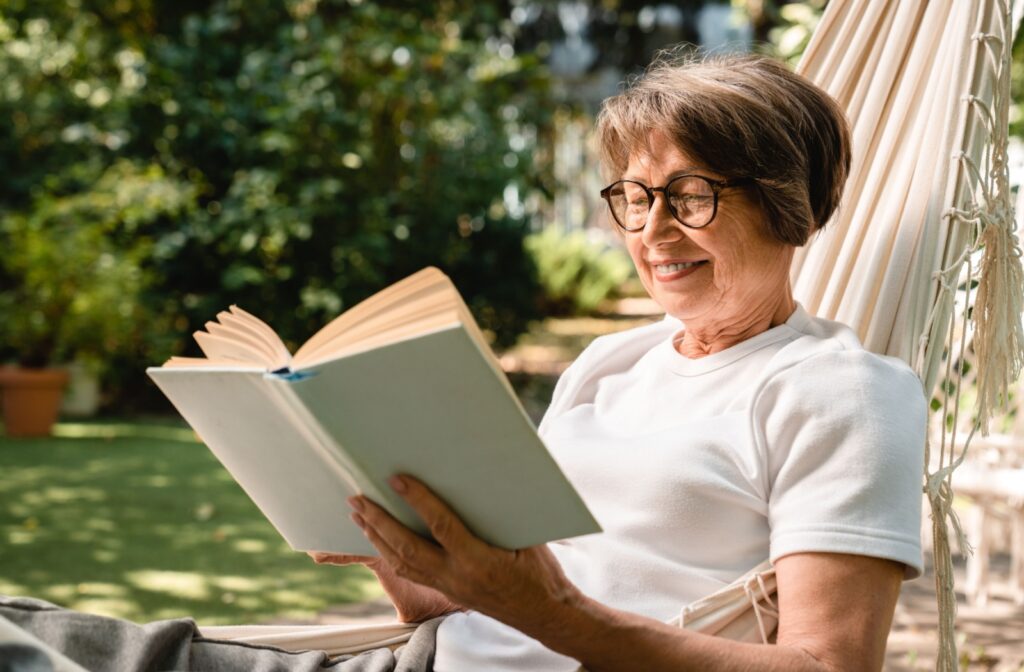 A happy adult sits outside and reads a book while enjoying the sunshine.