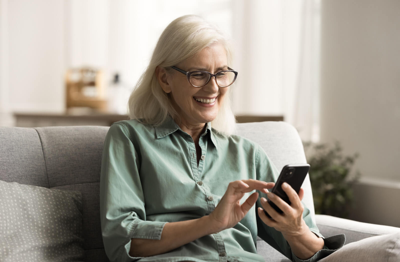 An older adult sitting on their couch in senior living, laughing while exploring the features on their new smart phone.
